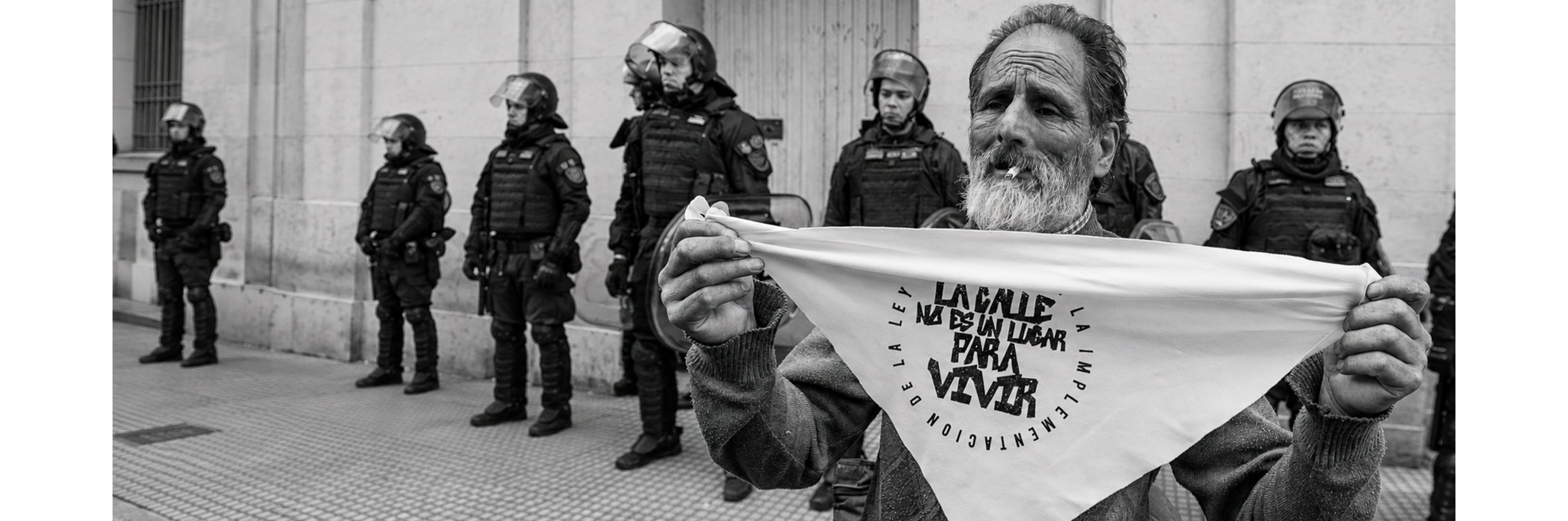 Un hombre sostiene un pañuelo con la leyenda "La calle no es un lugar para vivir" frente a un cordón policial, en una protesta por la implementación de la Ley de Situación de Calle. Foto: Natalia Bernades / La Retaguardia.